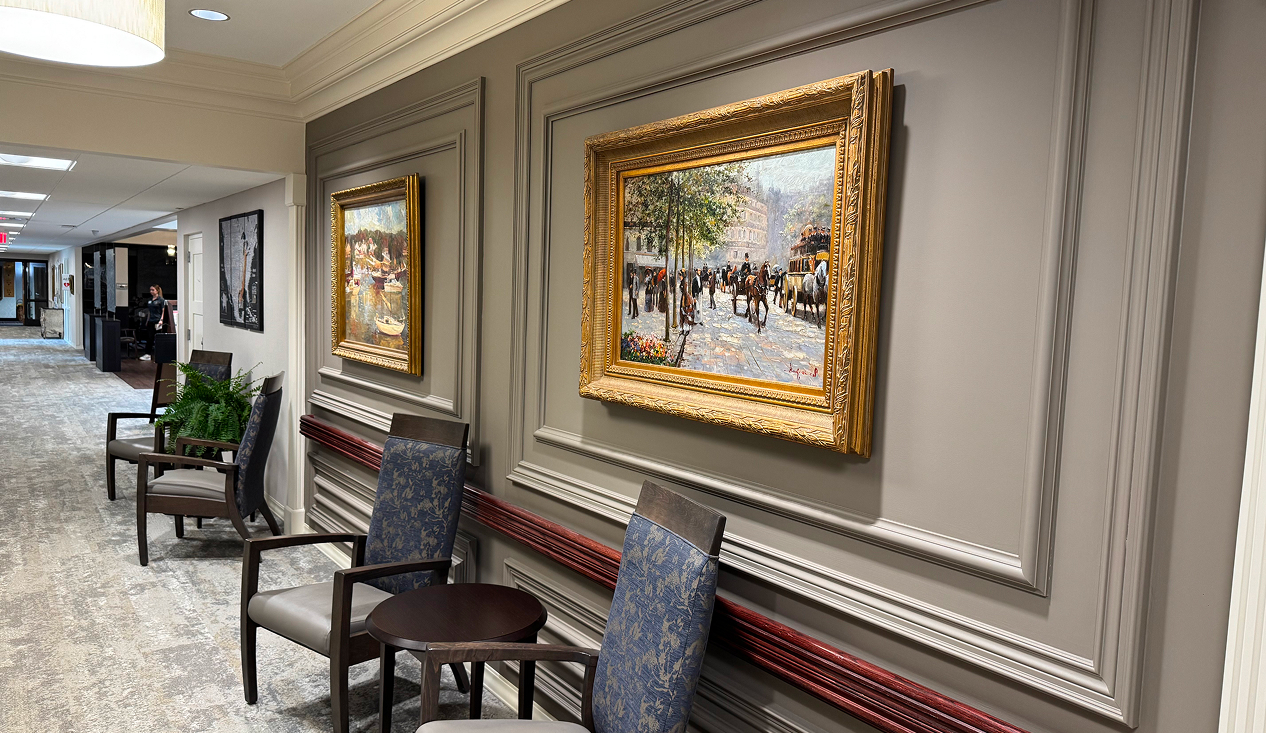 A hallway featuring chairs along the sides and colorful paintings hanging on the walls.