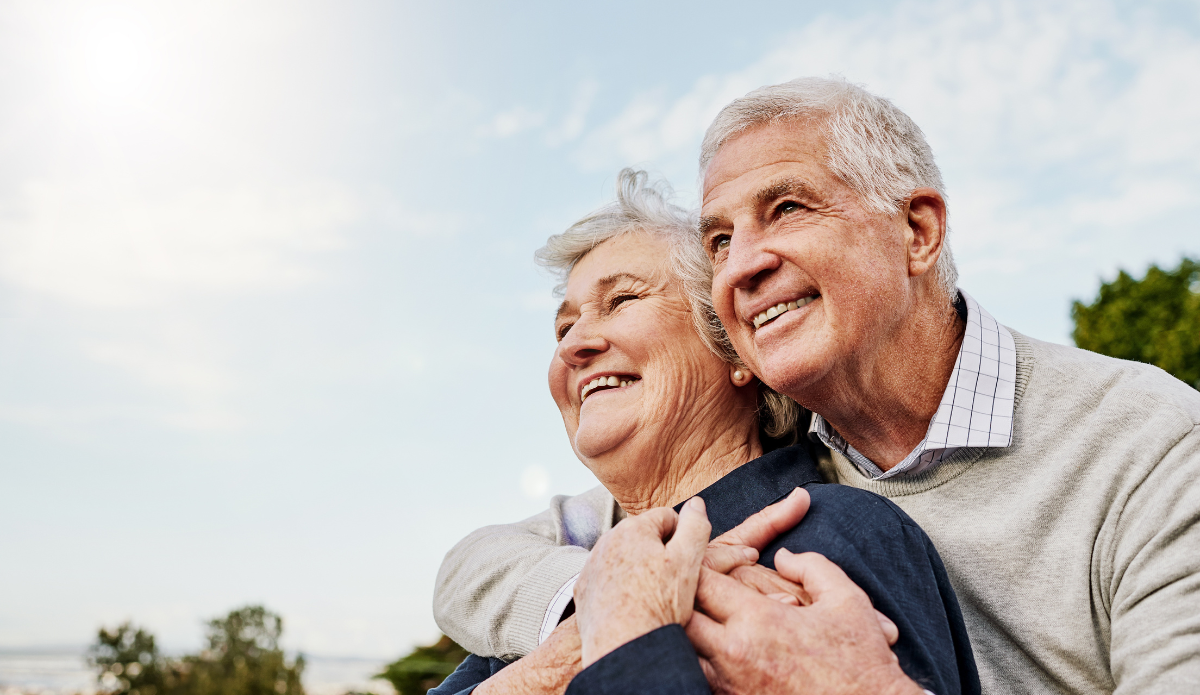 An elderly couple happily embracing each other while looking at afar